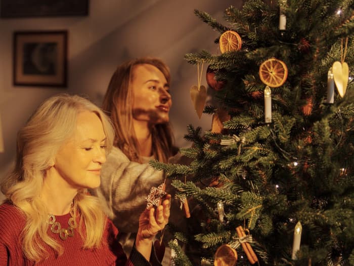 Mama und Tochter dekorieren den künstlichen Weihnachtsbaum FairyTrees FT33 bei warmem Abendlicht.