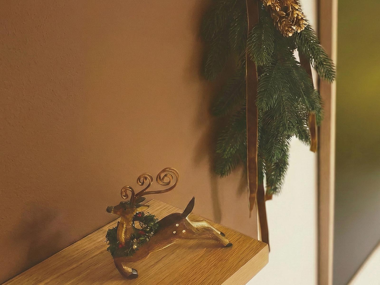 Im Flur h&auml;ngt eine Dekoration aus Zweigen eines k&uuml;nstlichen FairyTrees-Weihnachtsbaums und Tannenzapfen an der Wand und auf der Theke steht eine Rentierfigur.