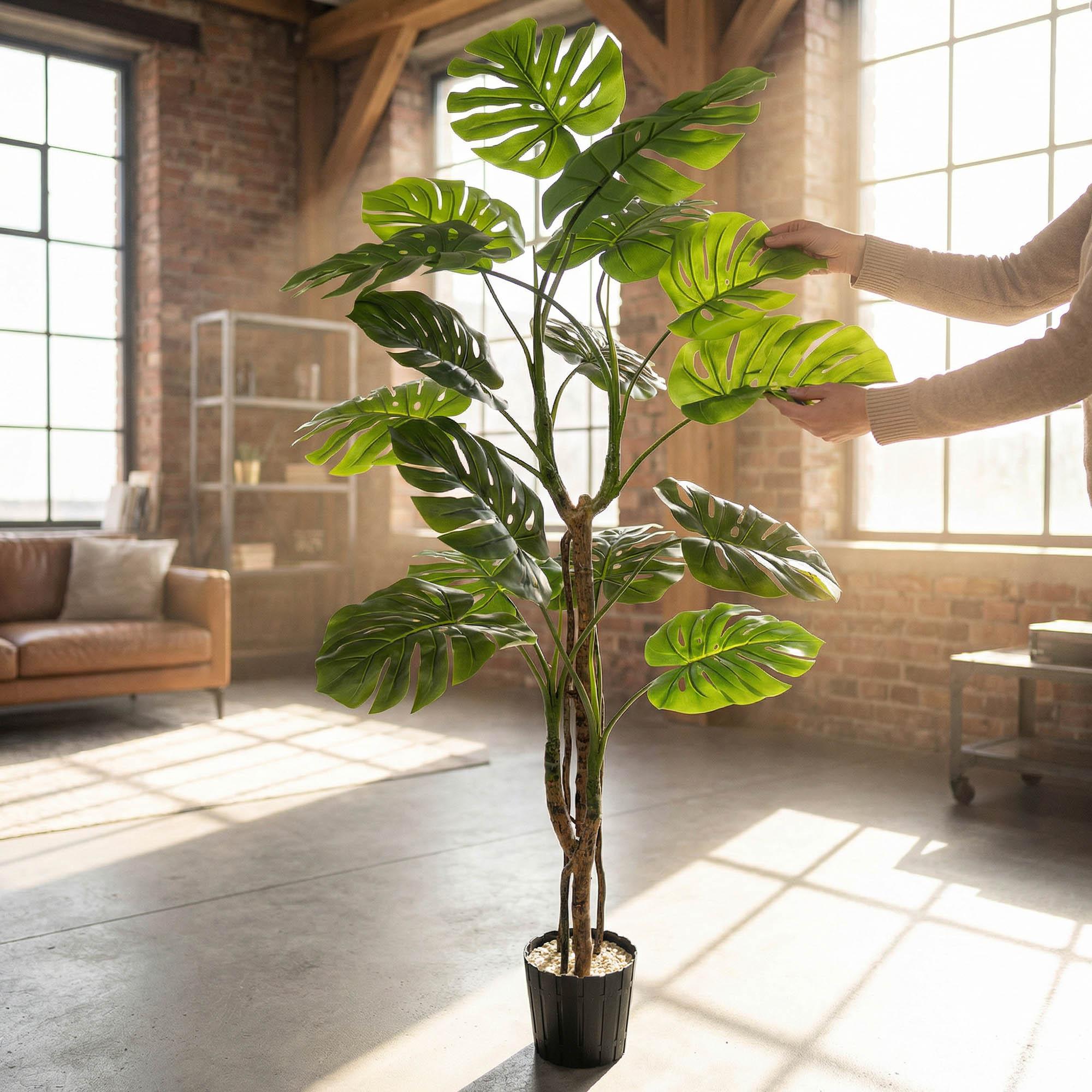 H&auml;nde richten die Bl&auml;tter der k&uuml;nstlichen Monstera auf einem 160 cm hohen Stiel von FairyTrees aus und betonen so ihr nat&uuml;rliches Aussehen und ihre Flexibilit&auml;t.